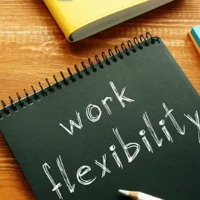 Flexibilité Texte noir sur fond bois : "work flexibility" écrit à la craie. Carnet et crayons en arrière-plan.